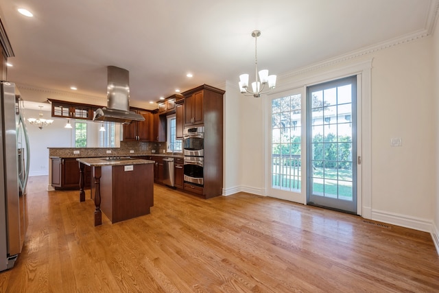 kitchen featuring island exhaust hood, hanging light fixtures, ornamental molding, and light wood-type flooring