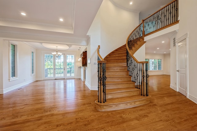 stairs with a wealth of natural light, hardwood / wood-style floors, a notable chandelier, and crown molding