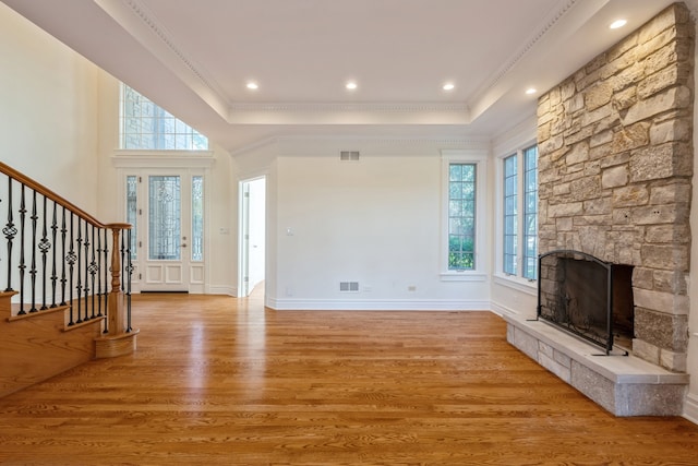 unfurnished living room with light wood-type flooring, a raised ceiling, a healthy amount of sunlight, and crown molding