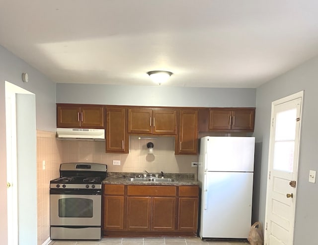 kitchen with backsplash, sink, light tile patterned floors, white fridge, and stainless steel range with gas stovetop