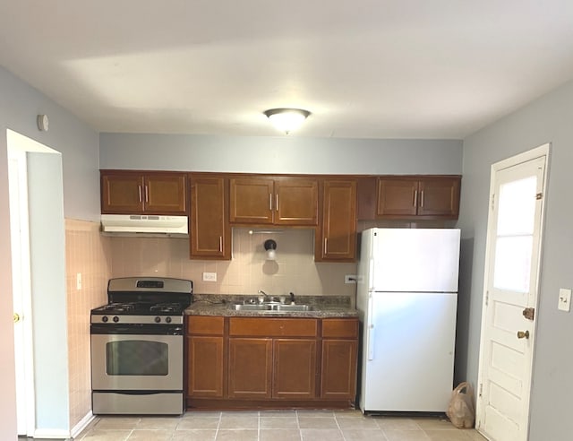 kitchen with light tile patterned flooring, backsplash, sink, white fridge, and stainless steel range with gas stovetop