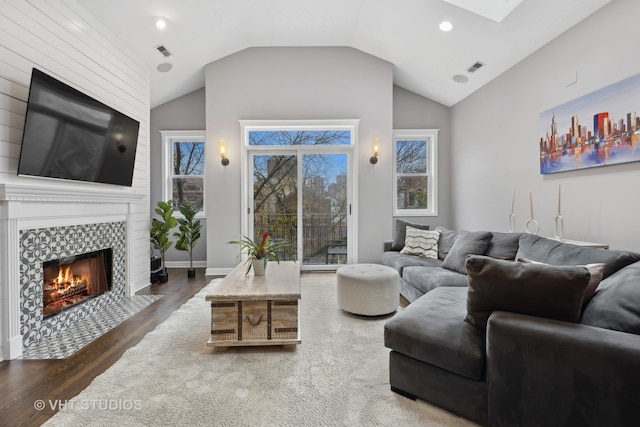 living room with dark wood-type flooring, vaulted ceiling, and a tile fireplace