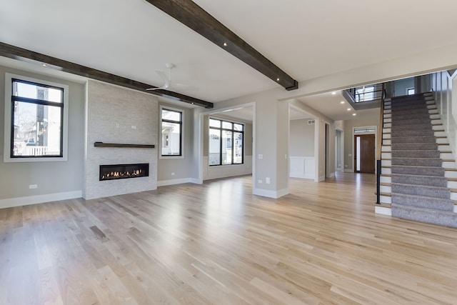 unfurnished living room with beamed ceiling, light wood-type flooring, a large fireplace, and ceiling fan