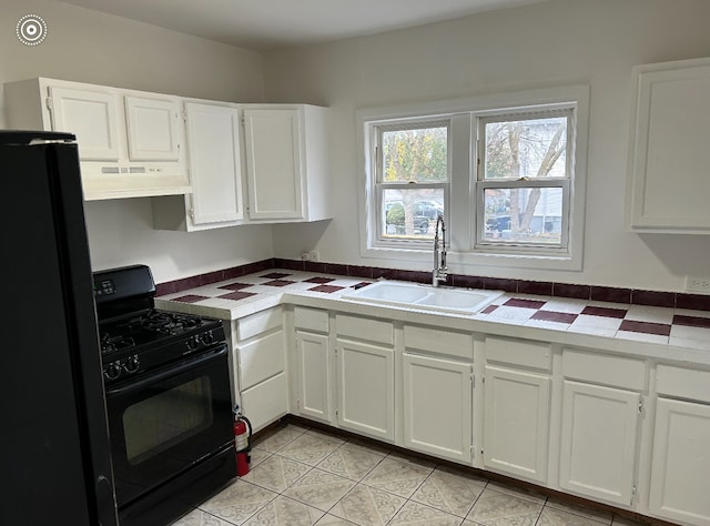 kitchen with black appliances, light tile patterned floors, sink, tile counters, and white cabinets