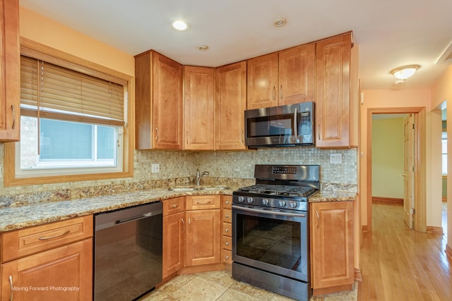 kitchen featuring sink, stainless steel appliances, light stone counters, light hardwood / wood-style flooring, and backsplash