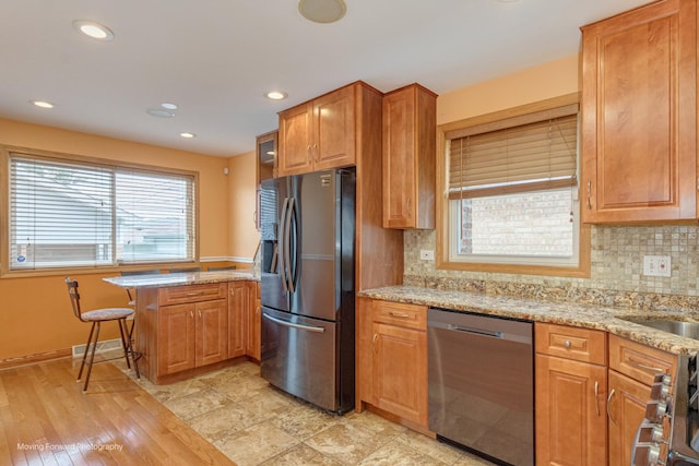 kitchen featuring decorative backsplash, appliances with stainless steel finishes, kitchen peninsula, light stone counters, and light hardwood / wood-style floors