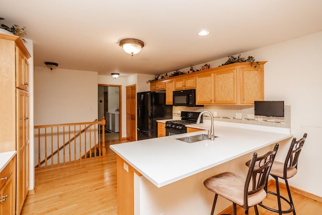 kitchen with sink, kitchen peninsula, light hardwood / wood-style floors, decorative backsplash, and black appliances