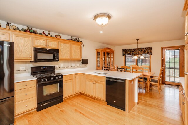 kitchen featuring black appliances, sink, hanging light fixtures, light hardwood / wood-style floors, and kitchen peninsula