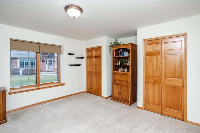 unfurnished bedroom featuring light colored carpet and multiple closets