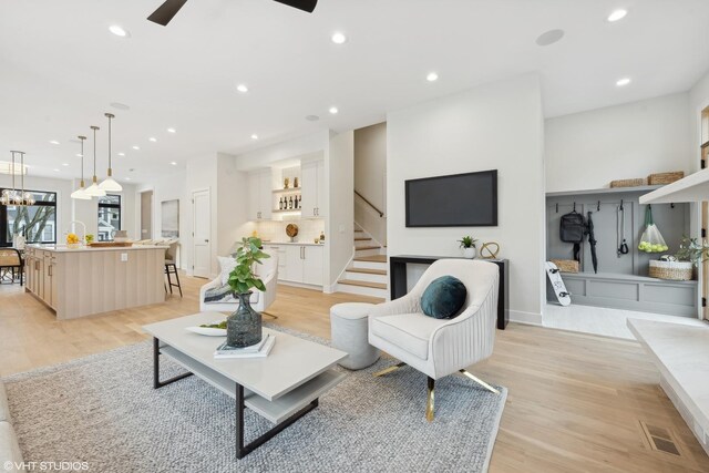 living room with ceiling fan with notable chandelier and light wood-type flooring