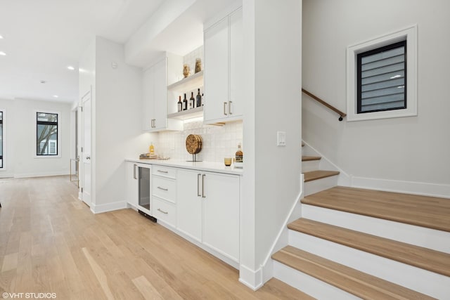 bar featuring wine cooler, decorative backsplash, light hardwood / wood-style floors, and white cabinets