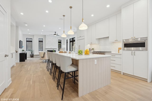 kitchen with pendant lighting, white cabinetry, stainless steel appliances, light hardwood / wood-style floors, and an island with sink