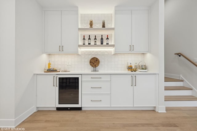 bar featuring wine cooler, white cabinetry, decorative backsplash, and light hardwood / wood-style flooring