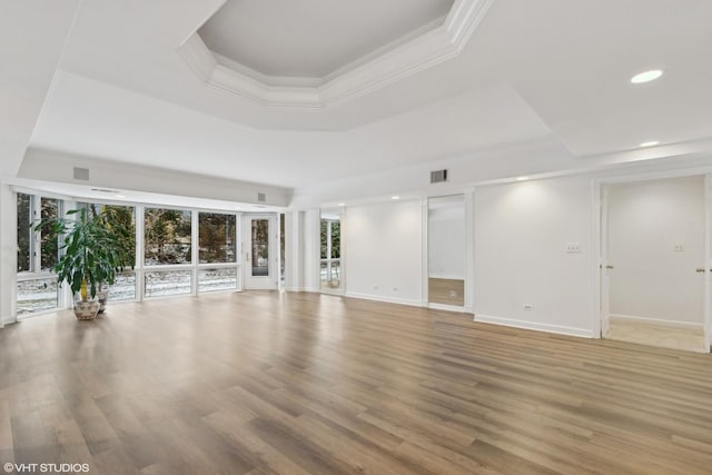 unfurnished living room featuring a tray ceiling, crown molding, and hardwood / wood-style floors