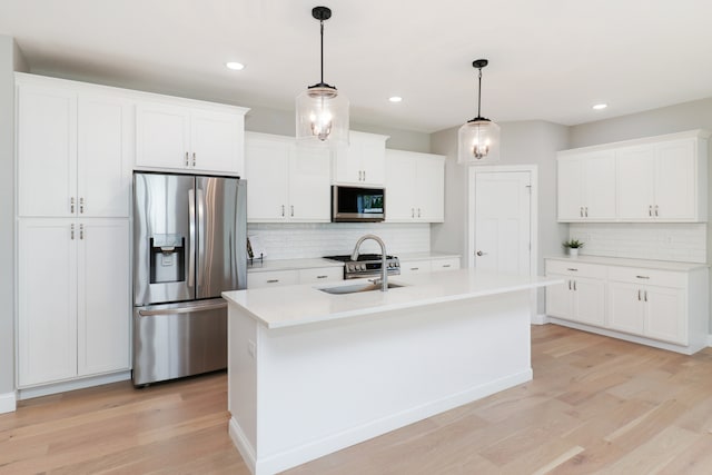 kitchen featuring hanging light fixtures, white cabinets, a kitchen island with sink, and appliances with stainless steel finishes