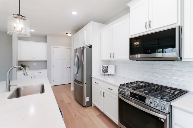 kitchen featuring stainless steel appliances, sink, decorative light fixtures, white cabinets, and light wood-type flooring