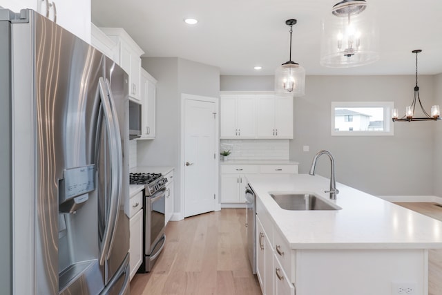 kitchen featuring stainless steel appliances, white cabinetry, decorative light fixtures, sink, and a kitchen island with sink