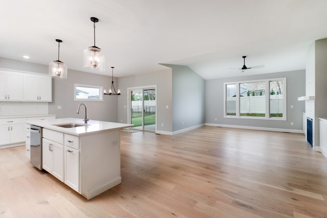 kitchen with a center island with sink, pendant lighting, sink, white cabinetry, and light hardwood / wood-style flooring