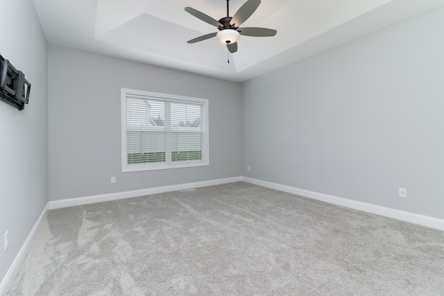 unfurnished room featuring a raised ceiling, light carpet, and ceiling fan