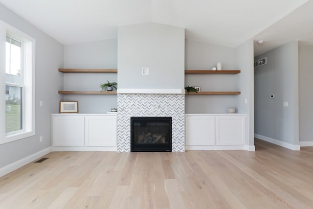 unfurnished living room with a tiled fireplace, plenty of natural light, and vaulted ceiling