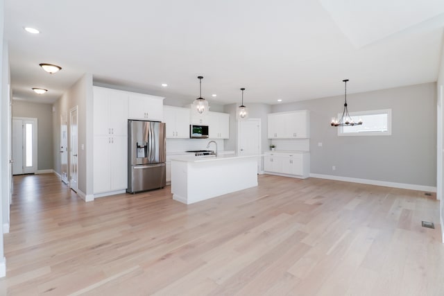 kitchen featuring a center island with sink, appliances with stainless steel finishes, light hardwood / wood-style floors, and hanging light fixtures