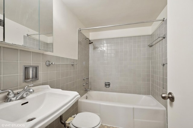 full bathroom with sink, tiled shower / bath combo, tile walls, and toilet