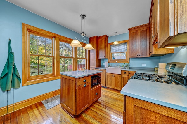 kitchen featuring sink, pendant lighting, light wood-type flooring, a kitchen island, and stainless steel range with gas stovetop