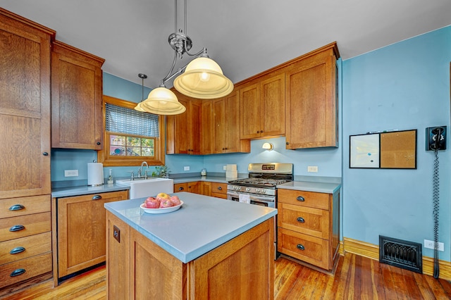 kitchen with gas stove, sink, light hardwood / wood-style floors, decorative light fixtures, and a kitchen island