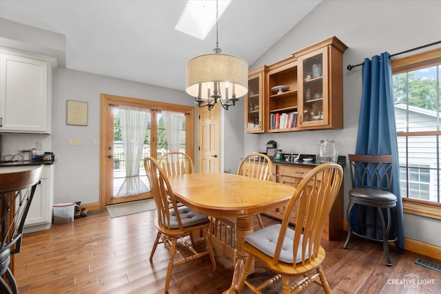 dining room with french doors, hardwood / wood-style flooring, an inviting chandelier, and vaulted ceiling with skylight