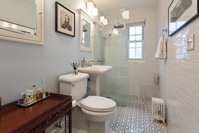 bathroom with tile patterned flooring, toilet, a tile shower, and radiator heating unit