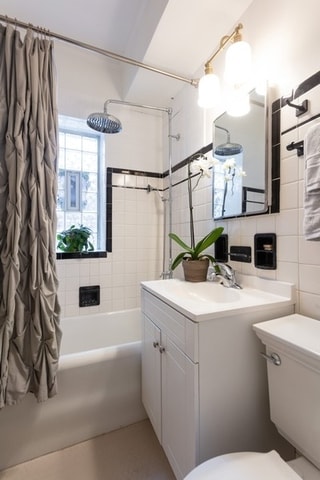 full bathroom with tasteful backsplash, toilet, shower / tub combo with curtain, vanity, and tile walls