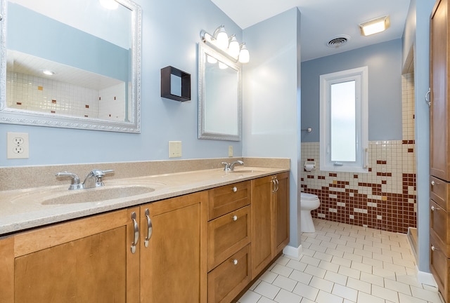 bathroom featuring tile patterned flooring, vanity, toilet, and tile walls