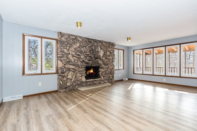 unfurnished living room with light wood-type flooring and a stone fireplace