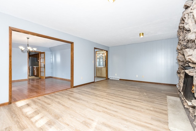 unfurnished living room featuring a fireplace, light wood-type flooring, and a chandelier