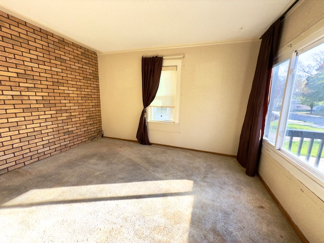 spare room featuring a textured ceiling, carpet flooring, and brick wall