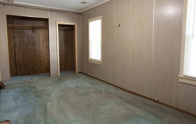 unfurnished bedroom featuring light colored carpet, wood walls, and multiple windows