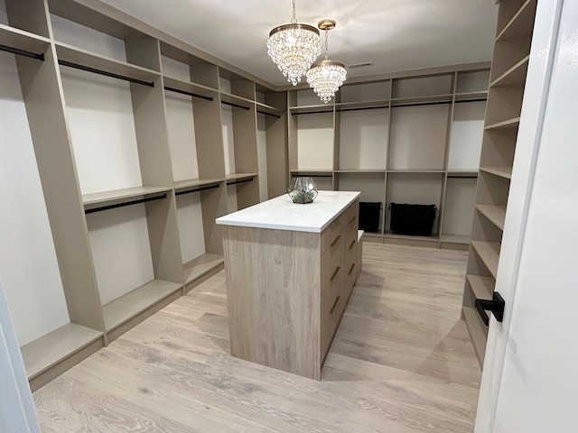 walk in closet with light hardwood / wood-style floors and an inviting chandelier