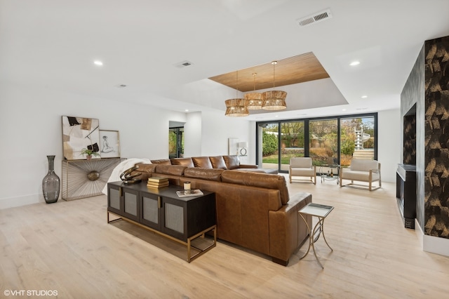 living room featuring a chandelier, a large fireplace, light hardwood / wood-style floors, and a raised ceiling