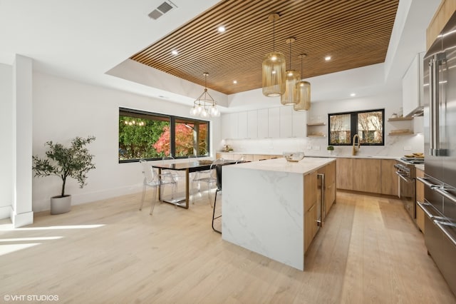 kitchen featuring high quality appliances, hanging light fixtures, a tray ceiling, a kitchen island, and light stone counters