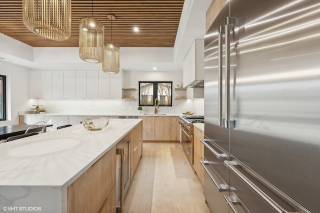 kitchen with light stone countertops, premium appliances, light hardwood / wood-style floors, pendant lighting, and a kitchen island