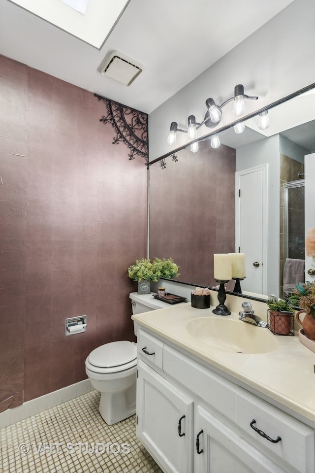 bathroom featuring vanity, a shower with door, a skylight, tile patterned flooring, and toilet