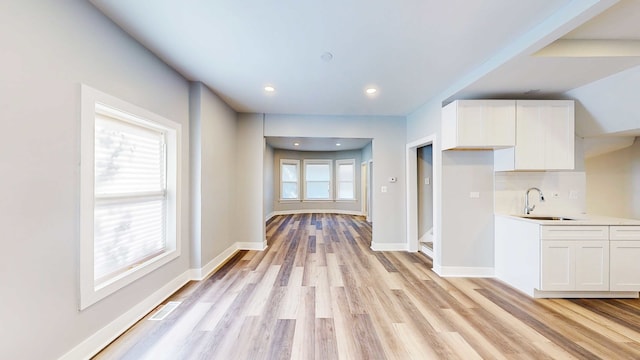 kitchen featuring white cabinets, light wood-type flooring, sink, and backsplash