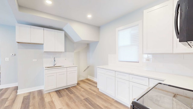 kitchen with stove, sink, backsplash, white cabinetry, and light wood-type flooring