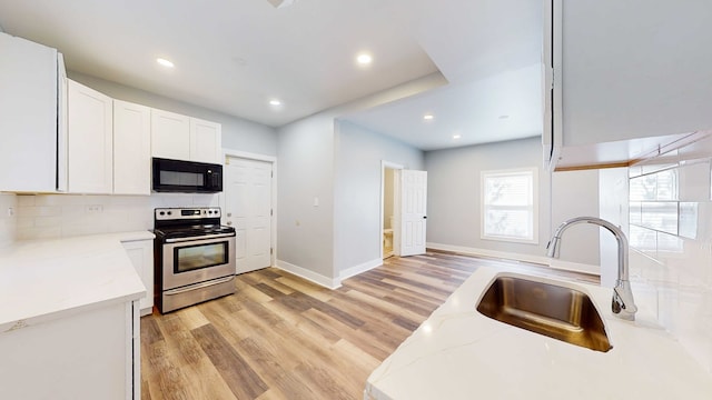 kitchen with white cabinetry, sink, light stone counters, stainless steel range with electric stovetop, and light wood-type flooring