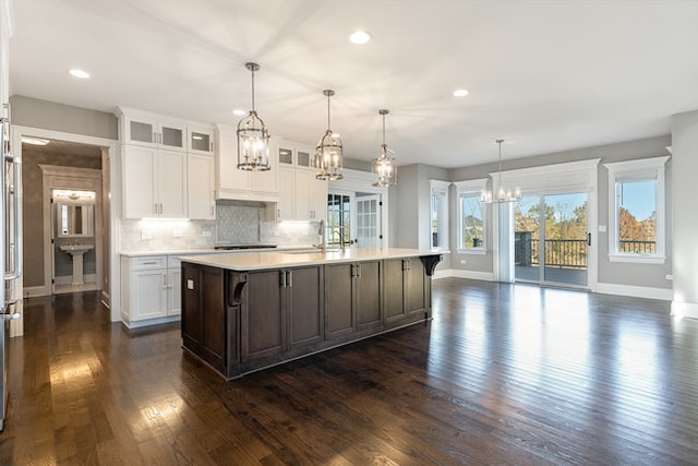 kitchen with a center island with sink, a breakfast bar area, hanging light fixtures, white cabinets, and dark wood-type flooring