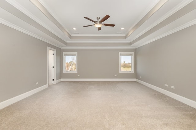 empty room with light colored carpet, ceiling fan, a tray ceiling, and ornamental molding