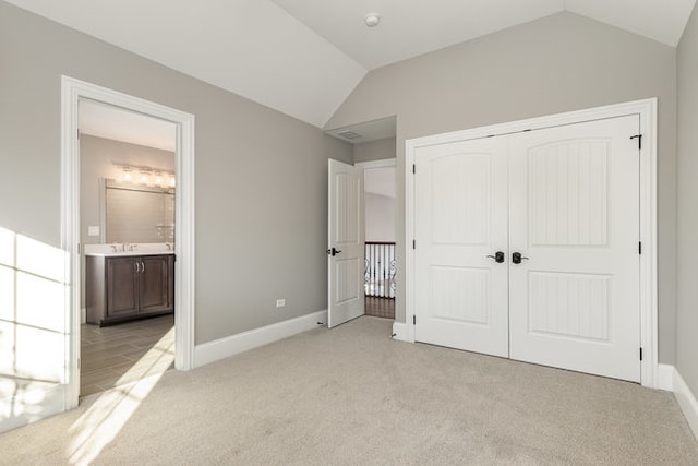 unfurnished bedroom featuring a closet, vaulted ceiling, light colored carpet, and ensuite bathroom