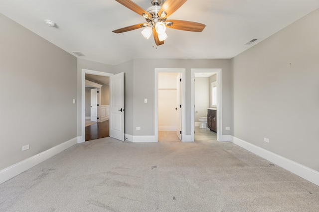 unfurnished bedroom featuring a closet, a walk in closet, connected bathroom, light carpet, and ceiling fan