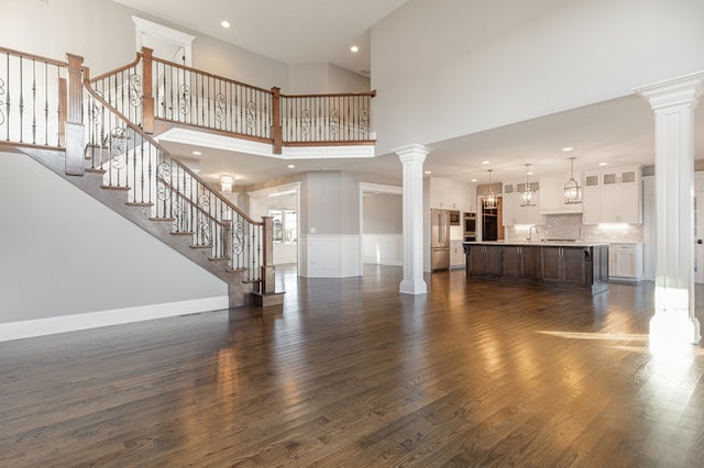 unfurnished living room featuring decorative columns, dark hardwood / wood-style floors, and a towering ceiling