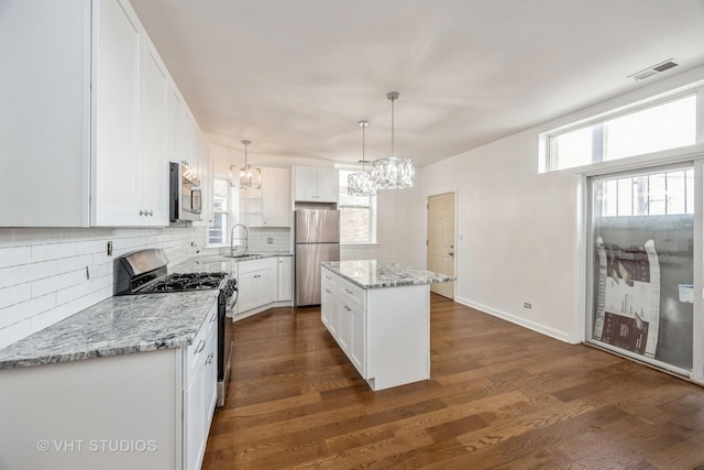 kitchen featuring visible vents, a kitchen island, hanging light fixtures, stainless steel appliances, and white cabinetry